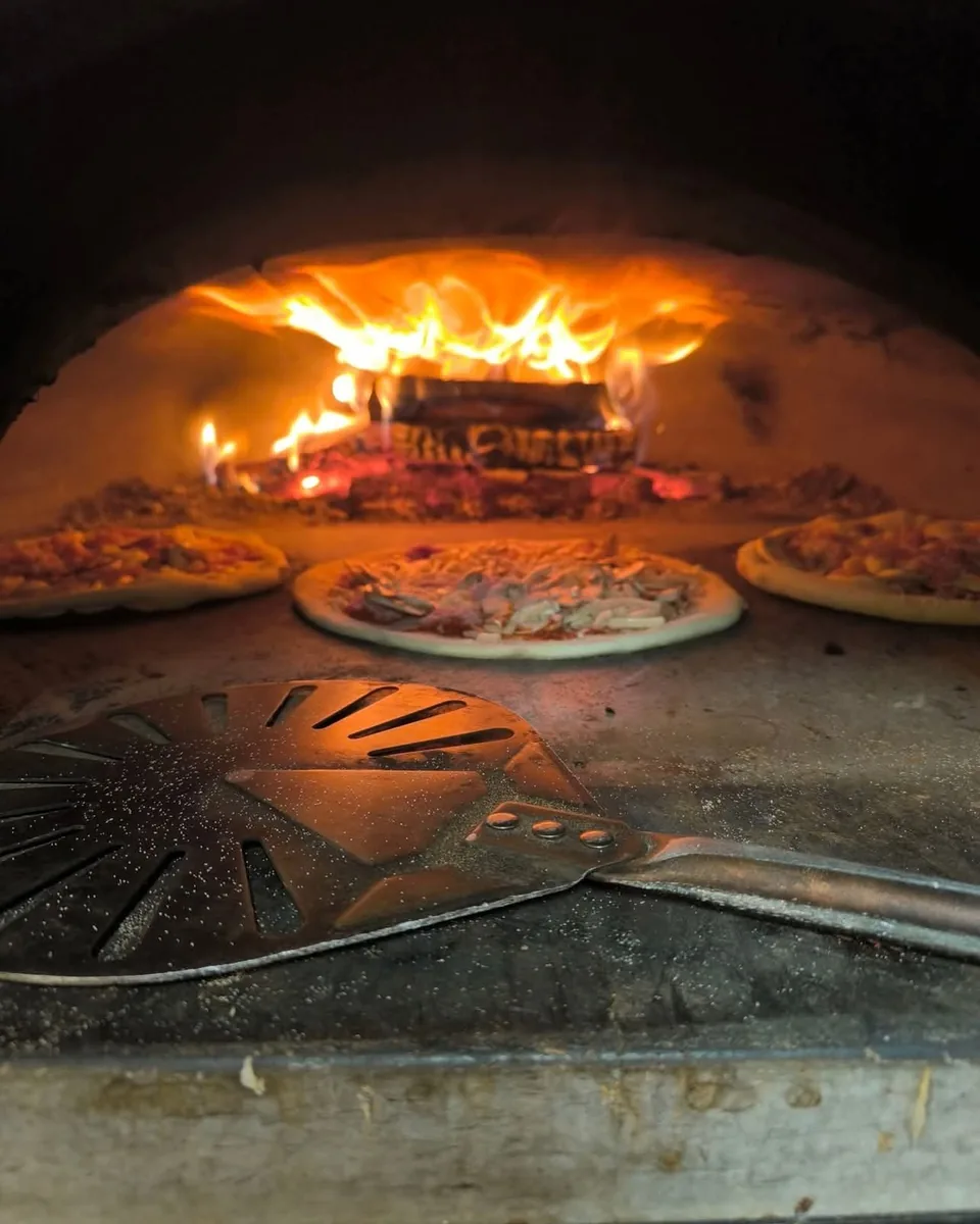 Deux pizzas en cuisson dans le four à bois du camion, flammes au fond